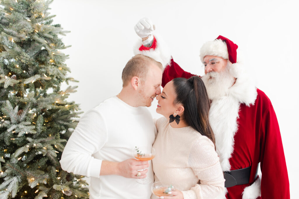 couple in front of a Christmas tree with Santa holding a mistletoe Miami Christmas Mini Session