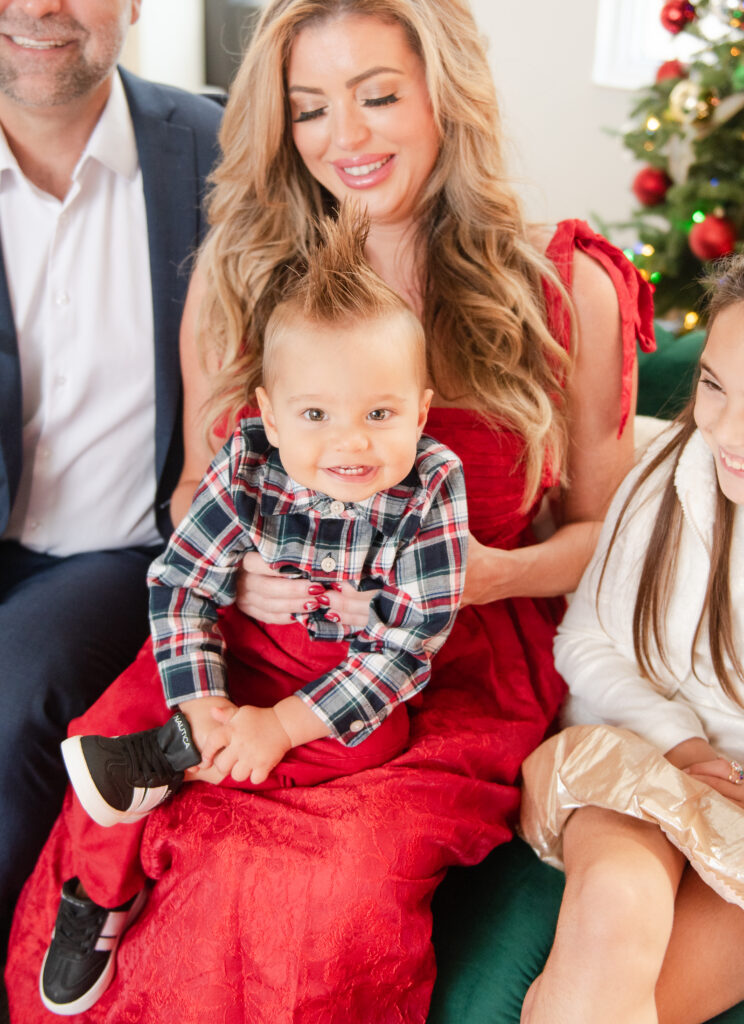 Mom holding one year old wearing red tartan at in home family Christmas pictures