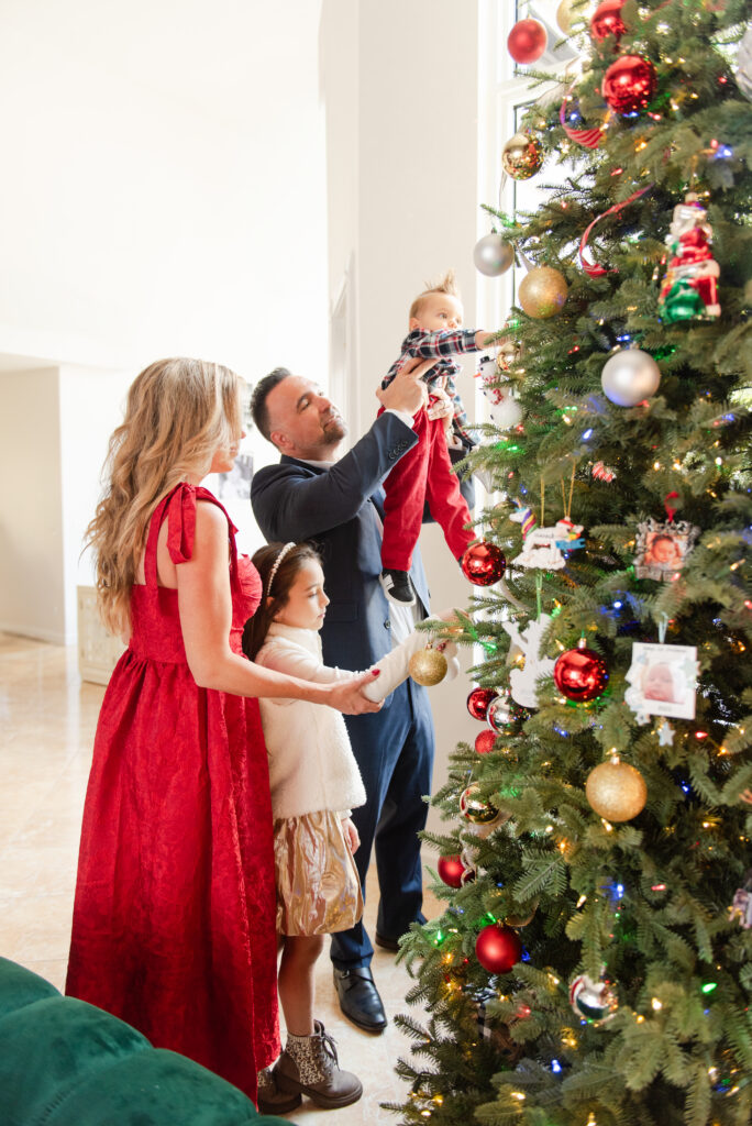 Family of four decorating a 12 ft Christmas Tree at in home Christmas family photo session