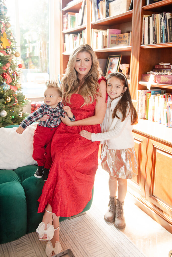 Mom with two kids in front of the Christmas tree and bookcase at an in home for christmas photoshoot by MSP Lifestyle Miami Family Photographers